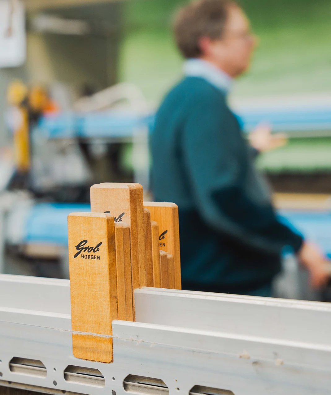 Detail van een weefmachine met houten onderdelen en een medewerker op de achtergrond