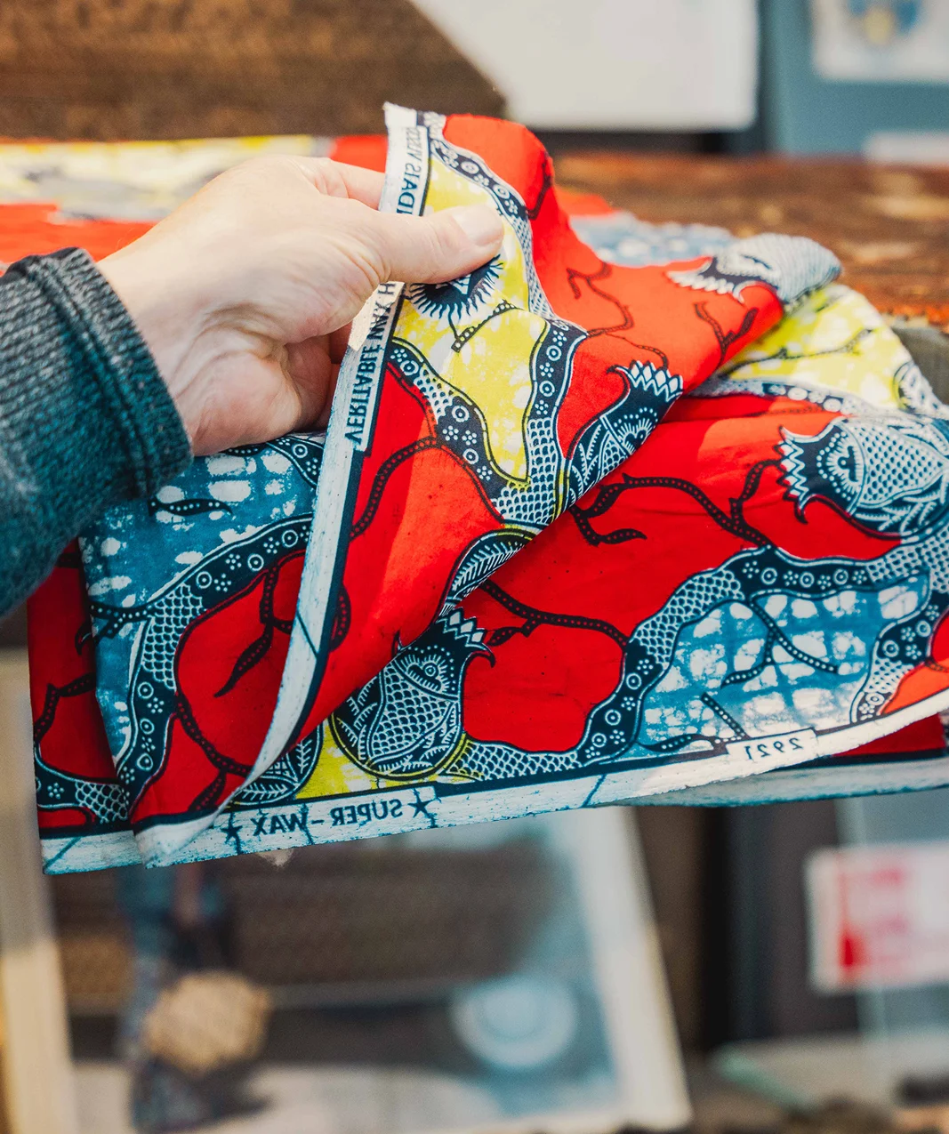 Hand toont kleurrijk bedrukt textiel met rode, blauwe en gele patronen.